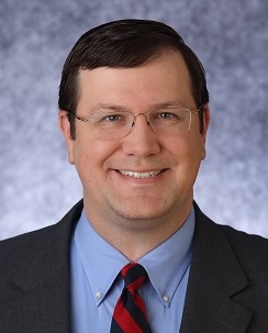 Portrait of David smiling in a suit and tie.