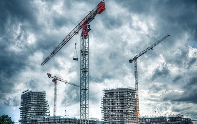 Construction cranes over buildings under a cloudy sky