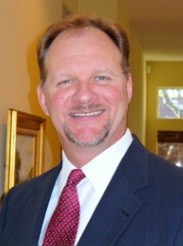 Smiling man with a goatee wearing a suit and red tie.