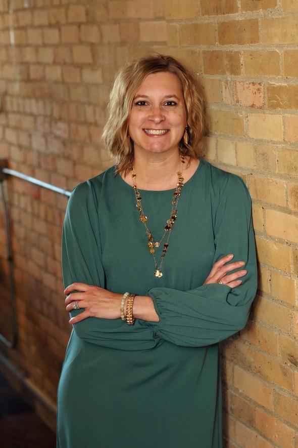 Professional woman smiling with arms crossed in front of a brick wall