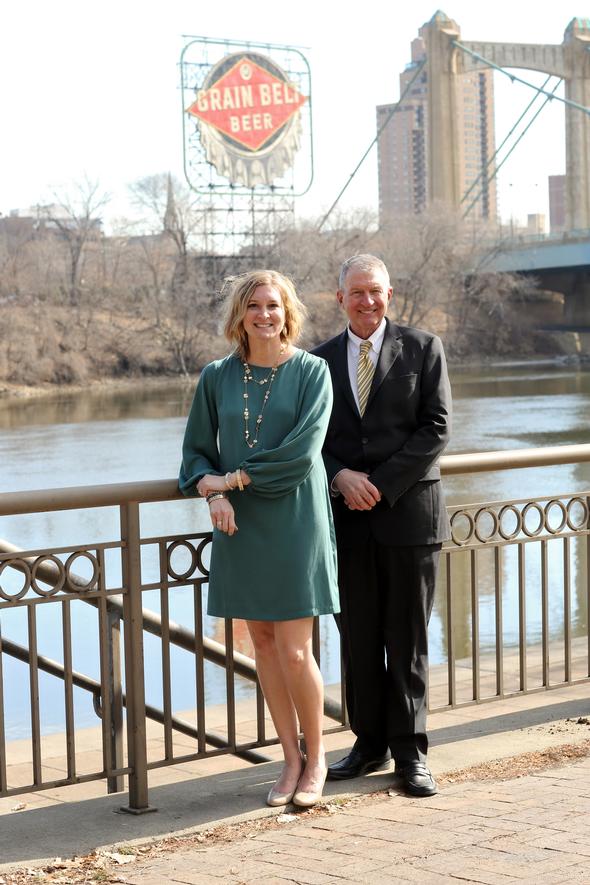 Professional man and woman posing near a river and bridge.