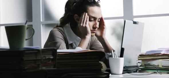 Stressed woman holding her head at a desk with a laptop.