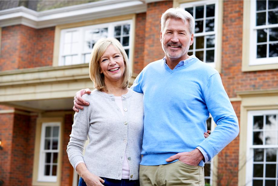 Smiling senior couple standing in front of their brick home