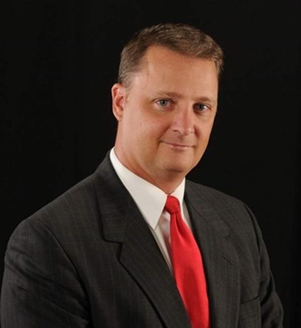 Professional headshot of a team member in a suit and red tie