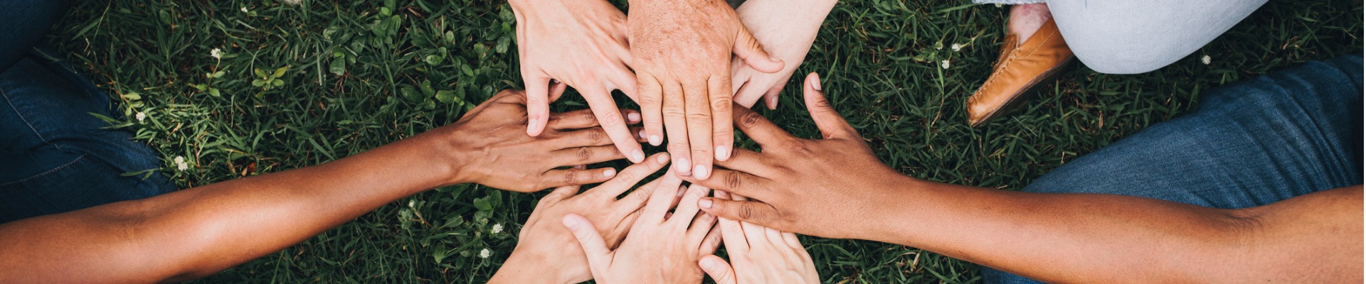 Diverse hands joined in a circle over green grass.