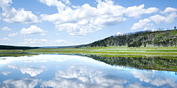 Reflection of white clouds in a calm blue lake by a green hill