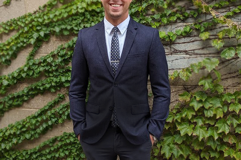 Smiling man in a dark suit against a vine-covered wall