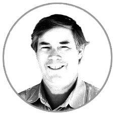 Black and white headshot of a smiling man in a circle frame