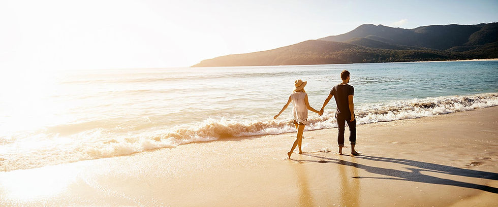Couple holding hands while walking on a sunny beach.