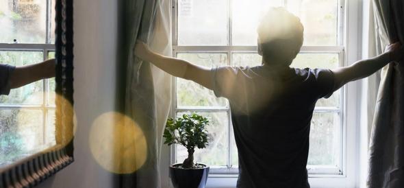 Man opening curtains to morning sunlight at a window