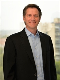 Smiling man in a black blazer and blue shirt.