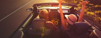 Couple in a convertible driving at sunset with arms raised