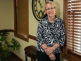 Smiling woman in patterned jacket leaning near a wall clock