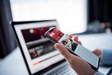 Person reading news articles on a smartphone near a laptop.