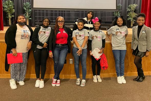 A group of girls and a mentor posing on a stage.