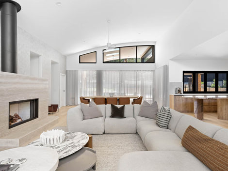 Open-plan living room with curved sofa, fireplace, marble coffee tables, timber kitchen and dining area.