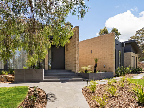 Front entrance with stone pathway, charcoal door, sandstone walls, and native garden beds.