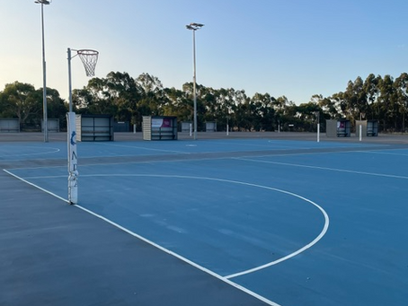Empty outdoor netball court at dusk with floodlights and gum trees in the background, Australia