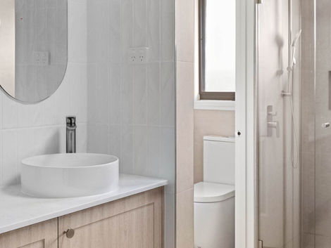 Bathroom with timber vanity, toilet, and glass shower in neutral tones.