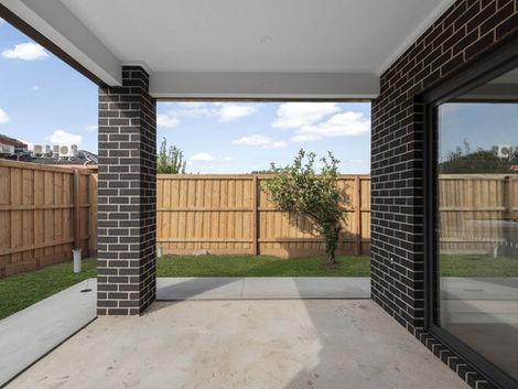 Alfresco area with dark brick columns, concrete floor, and view to fenced green lawn and small fruit tree.