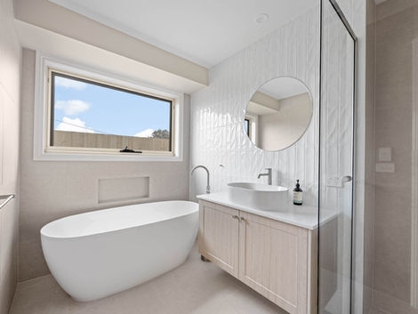 Modern bathroom with freestanding bath, round mirror, fluted tiles and timber vanity.