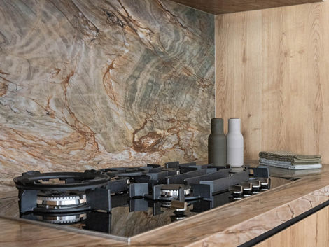 Detail of stone splashback and benchtop with gas cooktop and timber cabinetry.