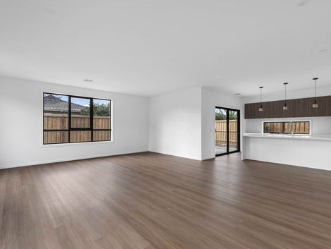 Spacious open-plan living area with timber floors, white walls, and kitchen view in the background.