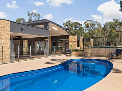 In-ground pool with sandstone walls, glass fencing, and covered alfresco entertaining area.