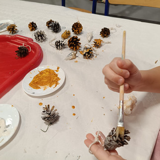 Dzieci malują złotą, srebrną i białą farbą szyszki sosnowe