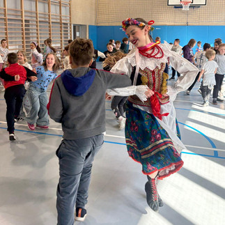 Tancerka w stroju ludowym prowadzi zajęcia taneczne z dziećmi na sali gimnastycznej.