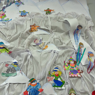 Pokolorowane sylwetki narciarzy i snowbordzistów przyczepione do udrapowanego z białego materiału stoku.