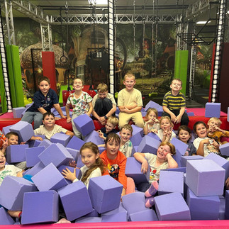 Grupa uśmiechniętych dzieci z klasy 1b pozuje razem w basenie z fioletowymi piankowymi klockami.