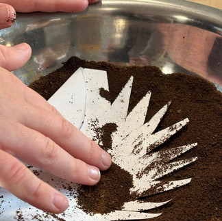 Dziecięca ręka obsypuje papierowego jeża fusami z kawy.