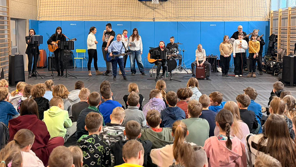 Występ muzyczny uczniów i nauczycieli z ZSS im. Matki Teresy z Kalkuty przed publicznością zgromadzoną na sali gimnastycznej.