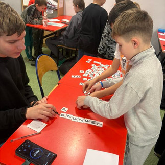 Uczniowie pochyleni nad ławką rozwiązują łamigłówki logiczne.