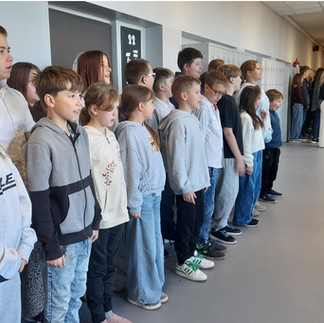 Grupa uczniów stojąca na baczność w szkolnym korytarzu, śpiewa hymn narodowy.