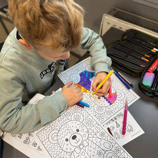 Uczeń pochylony nad pracą koloruje witraż z motywem misia.