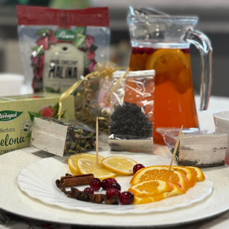 Torebki i pudełka z herbatą oraz talerzyk z plasterkami cytryny, pomarańczy, owocami żurawiny i laskami cynamonu.