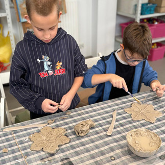 Uczniowie podczas warsztatów ceramicznych lepią z gliny śnieżynki.