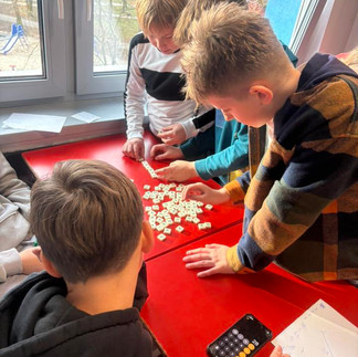 Uczniowie pochyleni nad ławką rozwiązują łamigłówki logiczne.