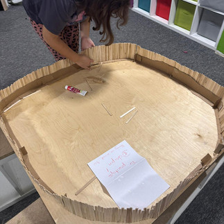 Dziewczynka pochylona nad makietą Biskupina - wzmacnia konstrukcję palisady obronnej wykonanej z drewnianych patyczków po lodach.