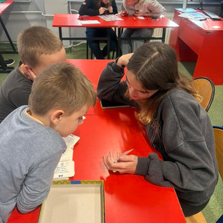 Uczniowie pochyleni nad ławką rozwiązują łamigłówki logiczne.