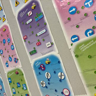 Plansze przedstawiające znaki drogowe, zawieszone na ściennej tablicy.