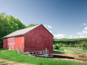 A red barn on top of a hillside overlooking a garden with mountains in the distance.