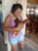 A woman looking down and smiling as she is holding a chicken.