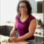 A smiling woman cutting vegetables on a cutting board in a well-lit kitchen.