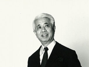 Black and white portrait of Yoshinobu Ashihara in formal attire, smiling and looking to his left. He has neatly combed white hair and a confident, warm expression.