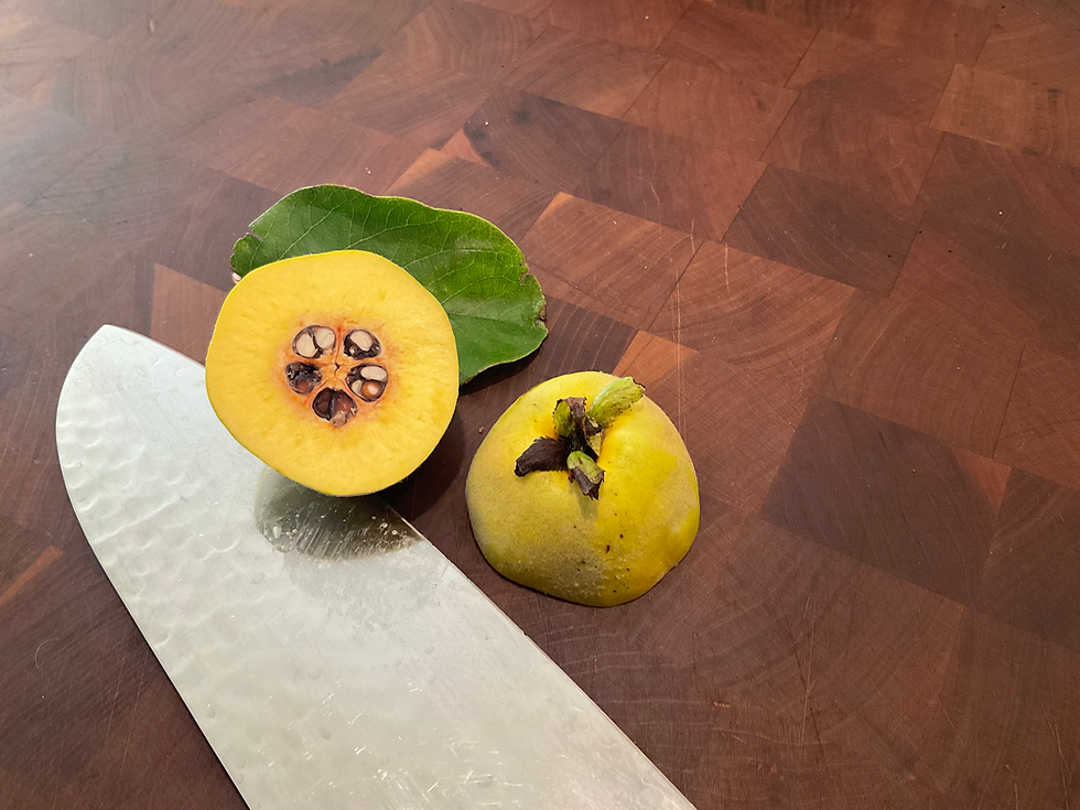 Halved quince fruit on a wooden cutting board next to a knife, showing yellow flesh and central seed cavity.