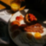 Breakfast plate with eggs, bacon, pancakes topped with strawberries, grapefruit slices, and a glass of orange juice. Sunlit, warm tone.