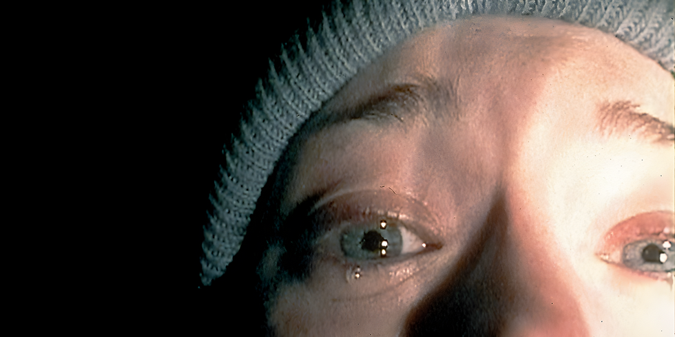 Close-up of a person’s face in a knit beanie, eyes open in dramatic light against a dark background.